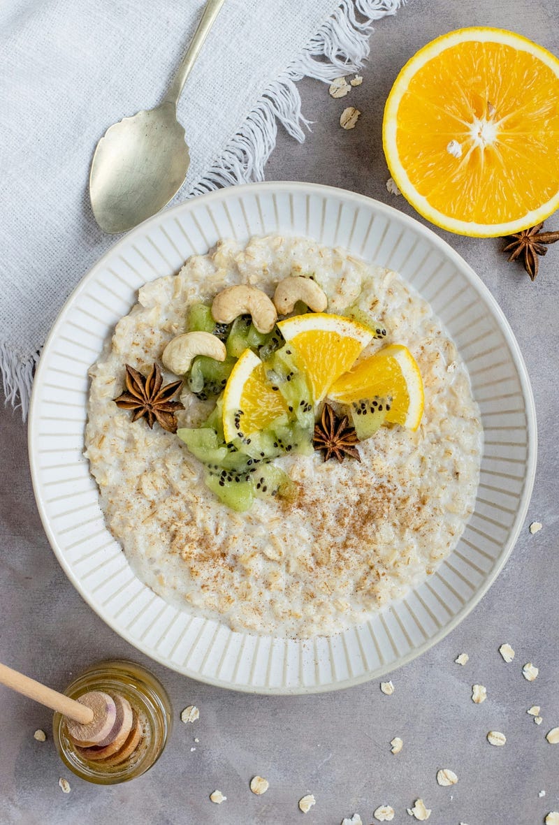 a bowl of oatmeal, or porridge, topped with cashews, kiwi fruit, orange wedges and star anise.